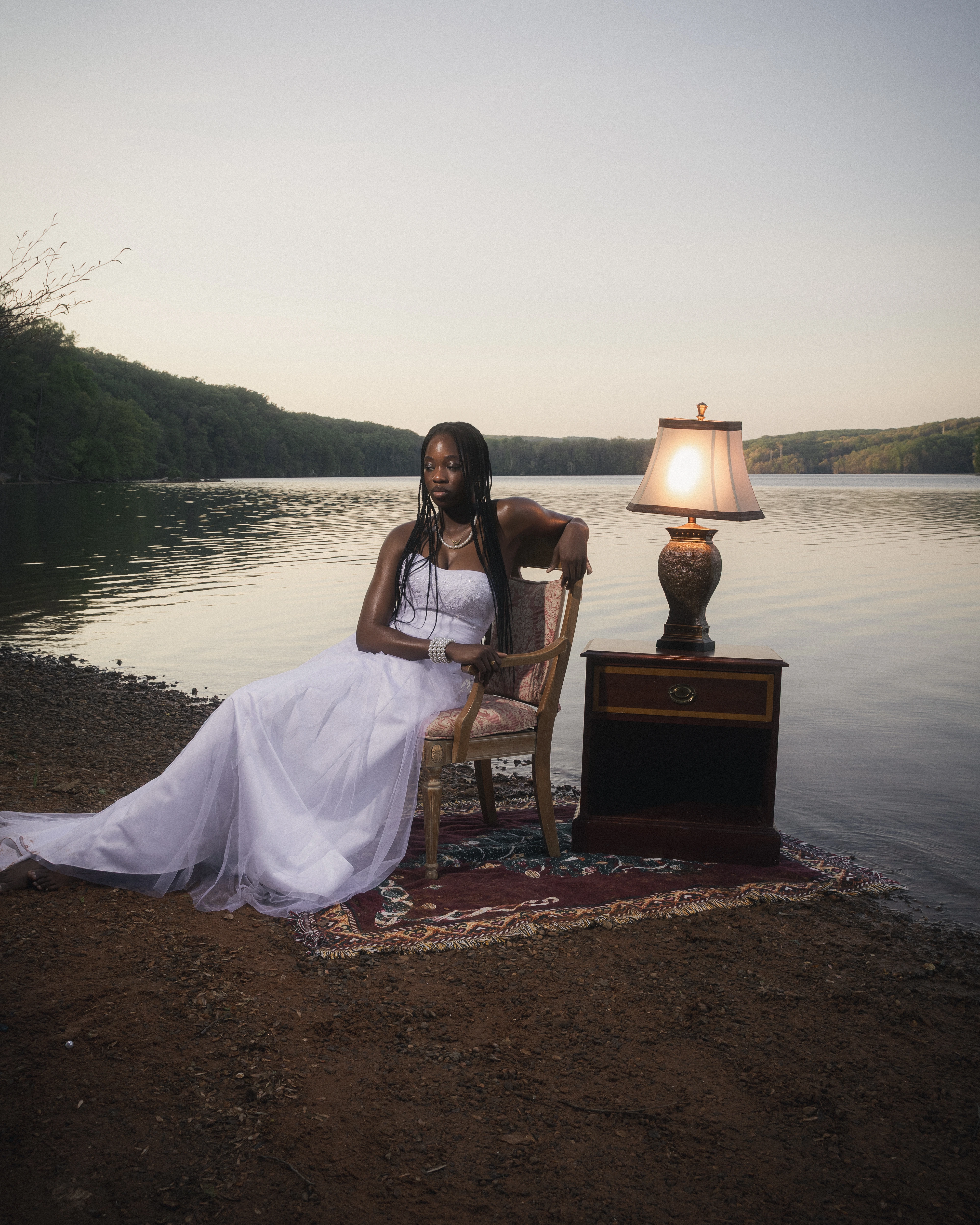 STILL editorial — model in cream gown leaning beside a vintage lamp at the riverside